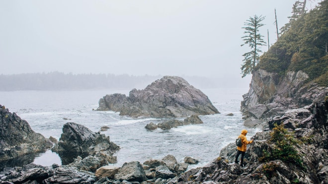 A lone figure navigates a rocky coastline.