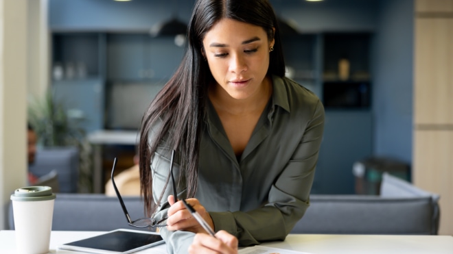 A woman writes notes at her desk.