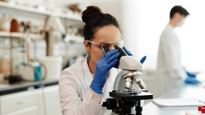 A woman in a laboratory looking down a microscope